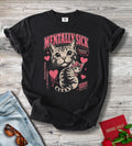 A black graphic t-shirt featuring a cat illustration and the text 'MENTALLY SICK' and 'SAVAGE SHELF' in pink and beige, styled in a flat-lay on a gray wood background with jeans, sunglasses, and a red book.