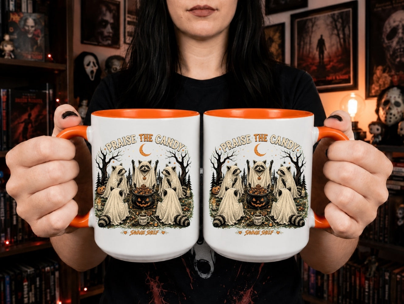 A person holds two white ceramic mugs with orange interiors and handles, featuring a Halloween graphic of three ghosts, a pumpkin, and the text 'Spinning the Candy' and 'Spinning the Cinnamon'. The background shows a cozy, dark-themed room with shelves and framed pictures.