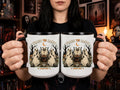 A person holds two white ceramic mugs with black interiors and handles, featuring a Halloween-themed illustration of three ghosts and the text 'I HATE THE CANDYCANES' with 'Jana 207' below. The background shows a cozy, dark room with bookshelves and framed pictures.